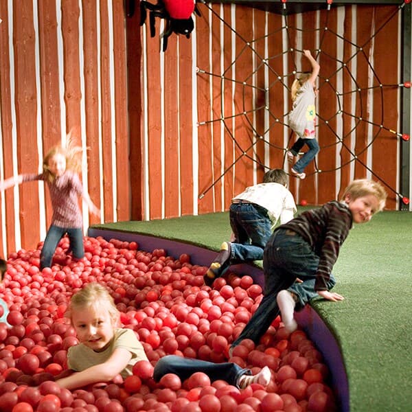 Djeca se igraju u dječjoj igraonici s penjalicama i bazenom punim crvenih loptica.