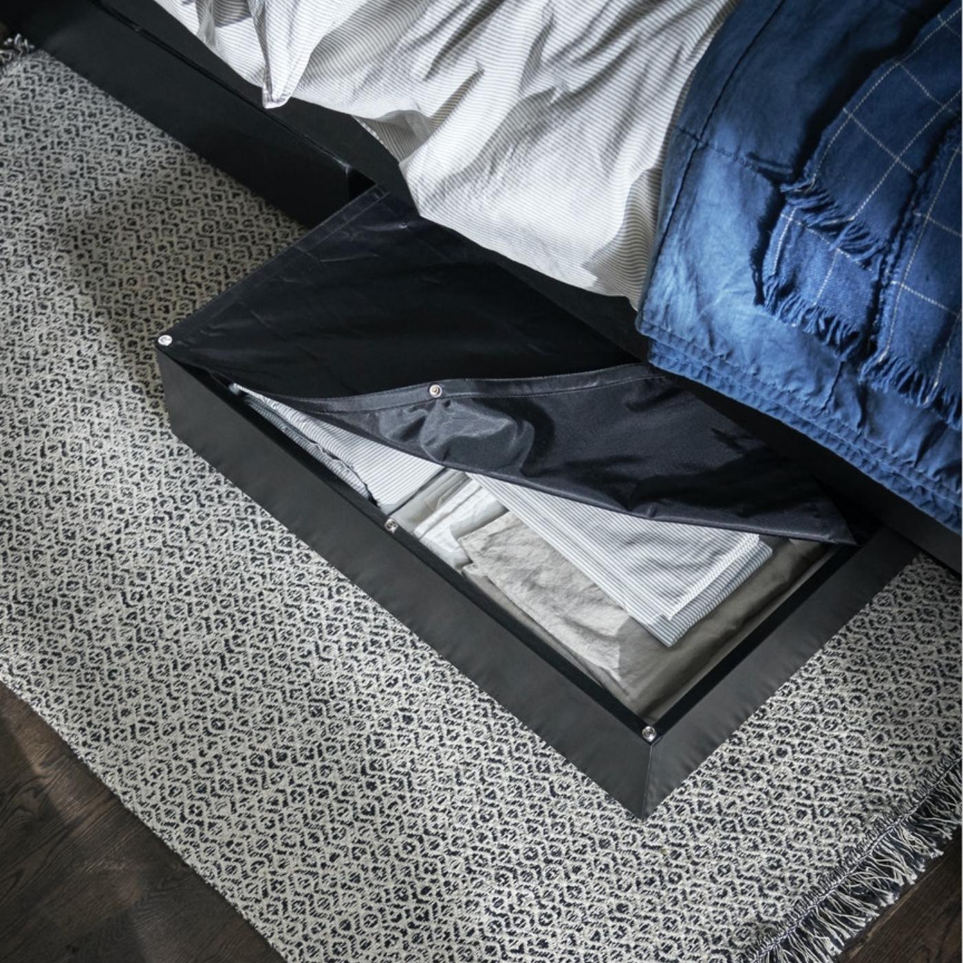 Djelomično otvorena LYCKSELE kutija za odlaganje viri ispod kreveta. U kutiji za odlaganje nalaze se uredno složeni tekstili.