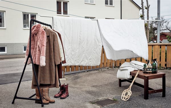 Dlážděný dvorek využitý pro jarní úklid: na šnůře visí přikrývky, na stojanu zimní kabáty, na zemi jsou zimní boty
