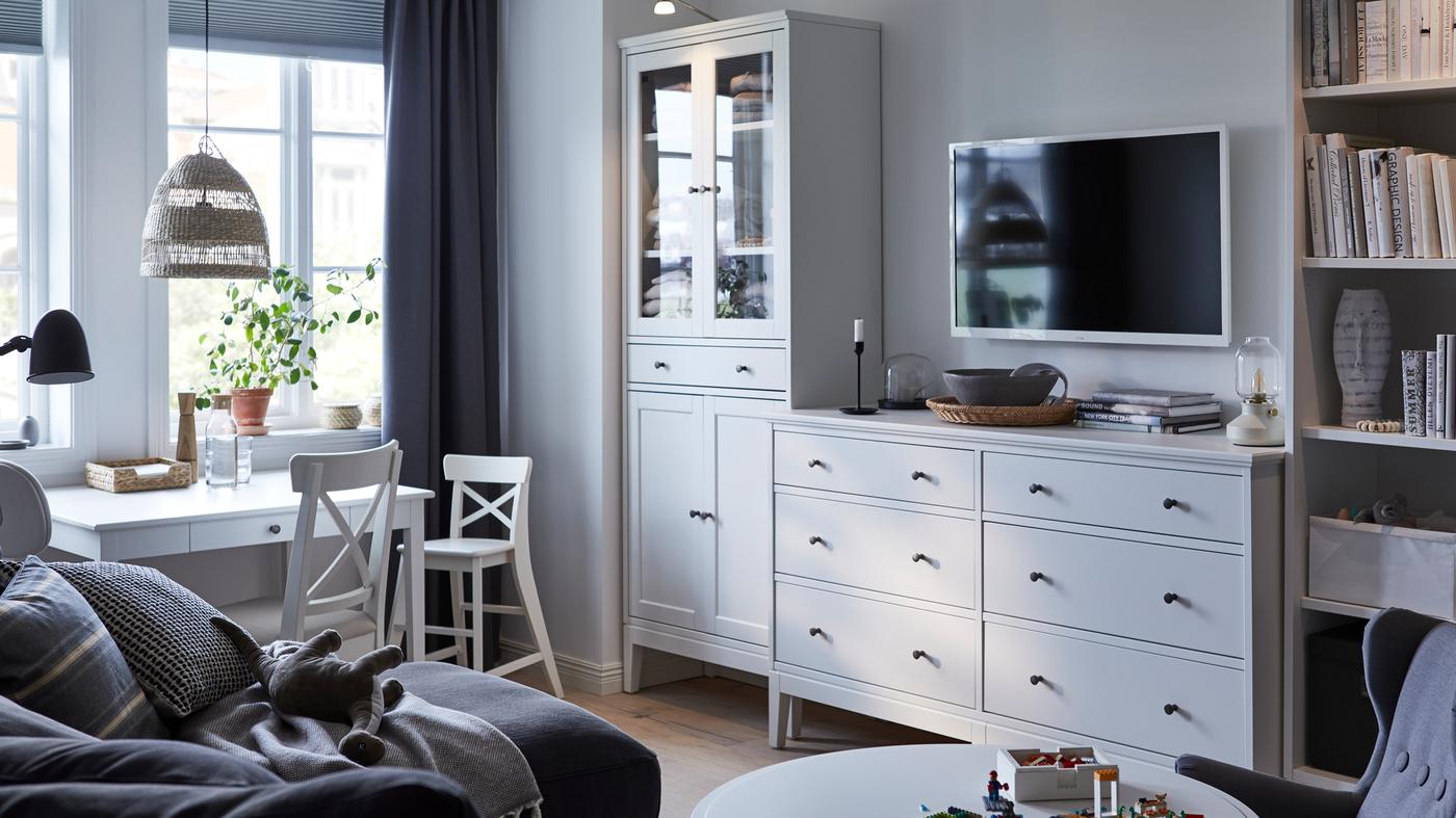 Dnevna soba v belih in sivih tonih, kjer ob steni stojijo IDANÄS vitrina, predalnik in knjižna omara.