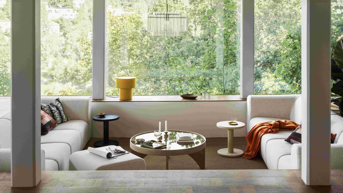 Dnevni boravak s bijelim kaučem, stolićima, knjigama, svijećama i velikim prozorima s pogledom na zelenilo.