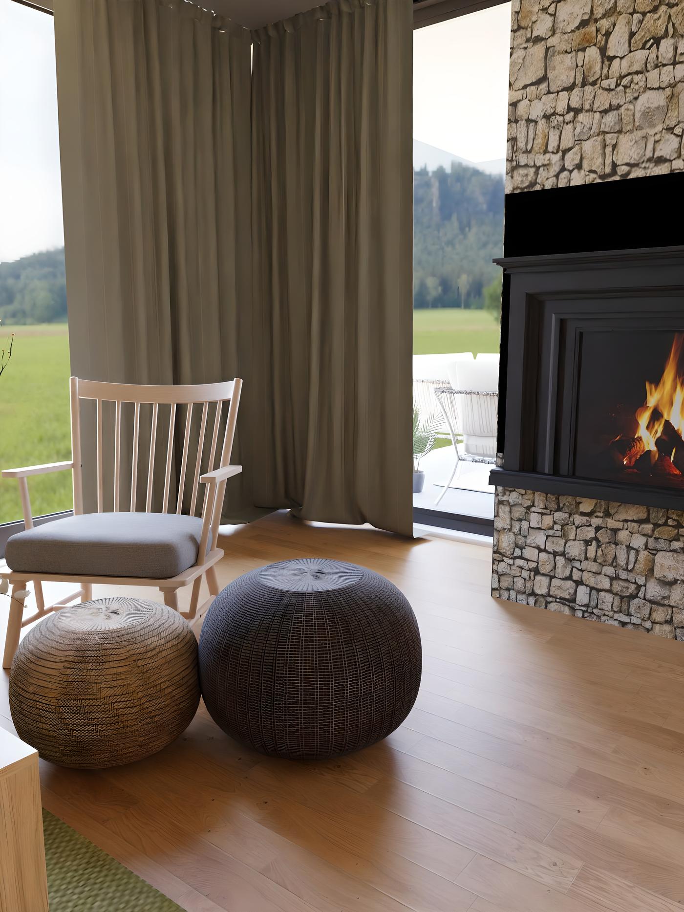 Dnevni boravak s kaminom, stolicom za ljuljanje, dva taburea i velikim prozorima s pogledom na prirodu.