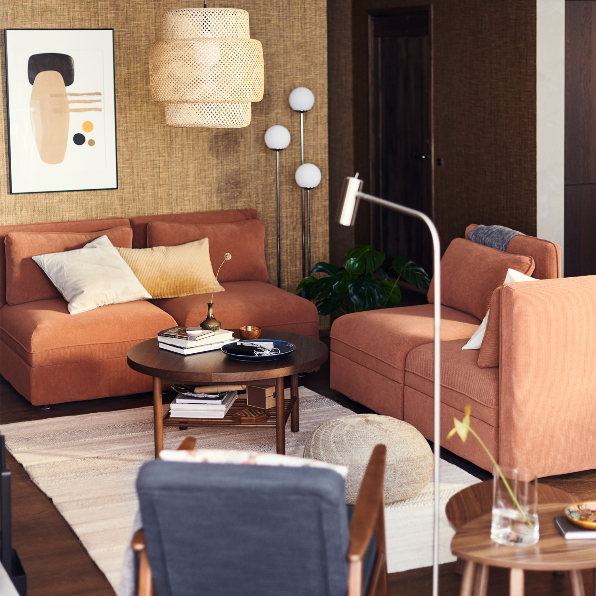 Dnevni boravak s VALLENTUNA modularnim sofama boje rđe ispod SINNERLIG visilice od bambusa.