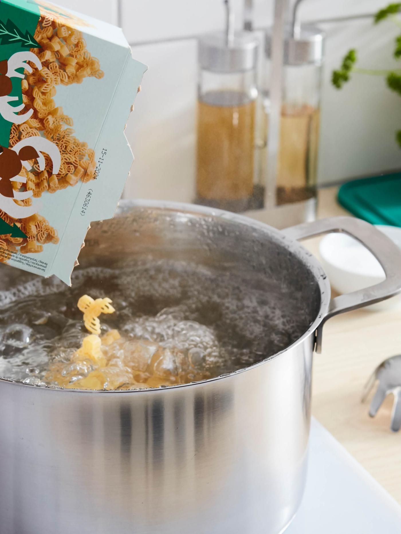 Do hrnce HEMKOMST plného vroucí vody padají z krabice těstoviny BÄSTISAR, které mají tvar losích hlaviček.