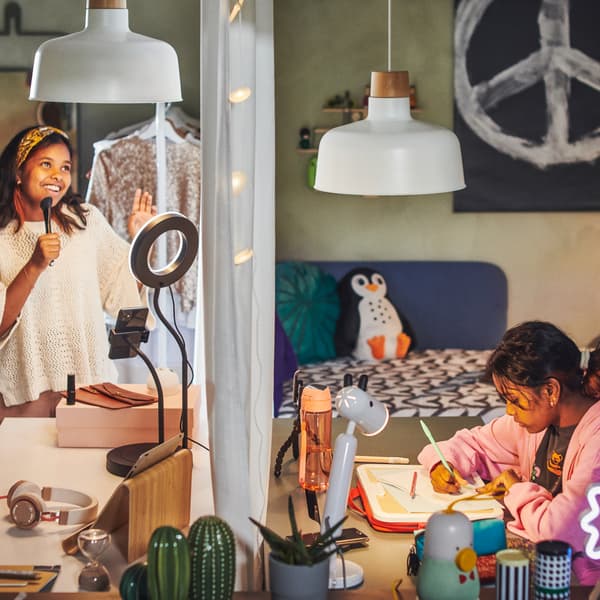 Doi copii într-un dormitor împărțit în două de o draperie. Unul dintre copii studiază la birou. Celălalt râde.