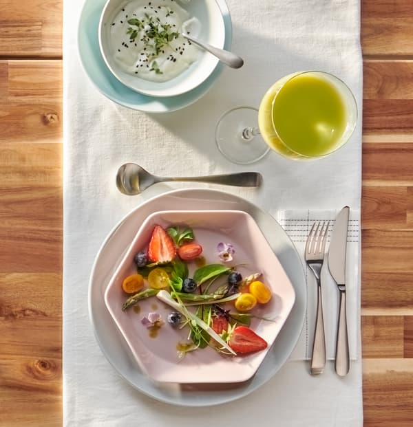 Dois pratos redondos, em cinzento e azul claro, uma taça branca e um prato rosa hexagonal FORMIDABEL com uma salada de verão.