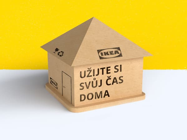 Domeček IKEA na žlutošedém pozadí sestavený z kartonu a s textem: "Užijte si svůj čas doma."
