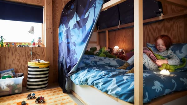 子ども部屋に、恐竜がモチーフのブルーテントとブルーの掛け布団カバーを使ったホワイトのKURA/キューラ リバーシブルベッド。その中でくつろいでいる子ども。