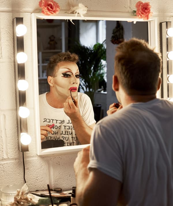 Donald applies make-up at his dressing table in front of a mirror with lights around the edges.