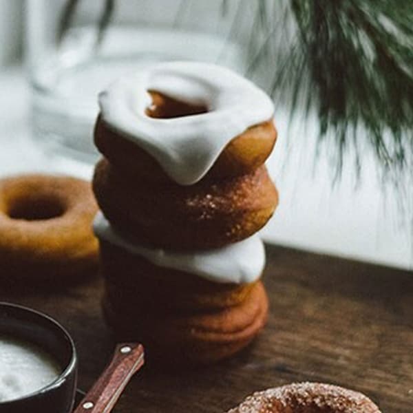 Donuts med vit glasyr staplöade på varandra på skärbräda i trä. 