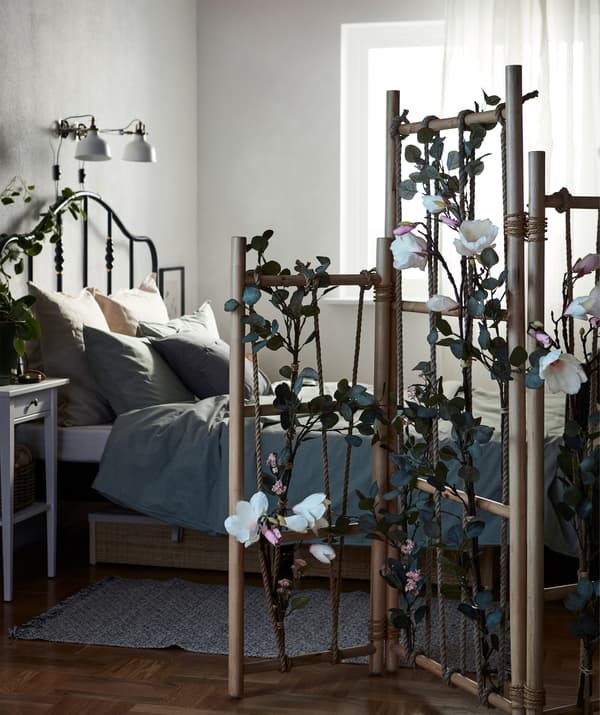 Dormitor cu pat împărțit cu ajutorul unui separator de cameră TÄNKVÄRD, îmbogățit și evidențiat cu ajutorul plantelor artificiale.  