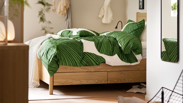 Dormitori amb llit de la sèrie TONSTAD en xapa de roure, amb emmagatzematge inferior i roba de llit verda amb estampat de fulles.