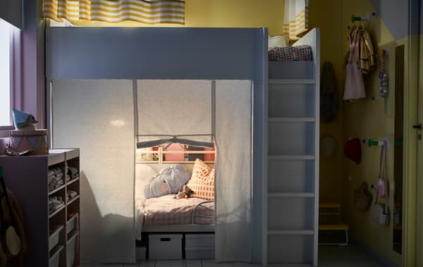 Dormitori infantil compartit amb un llit alt i un llit extensible a sota amb cortines.