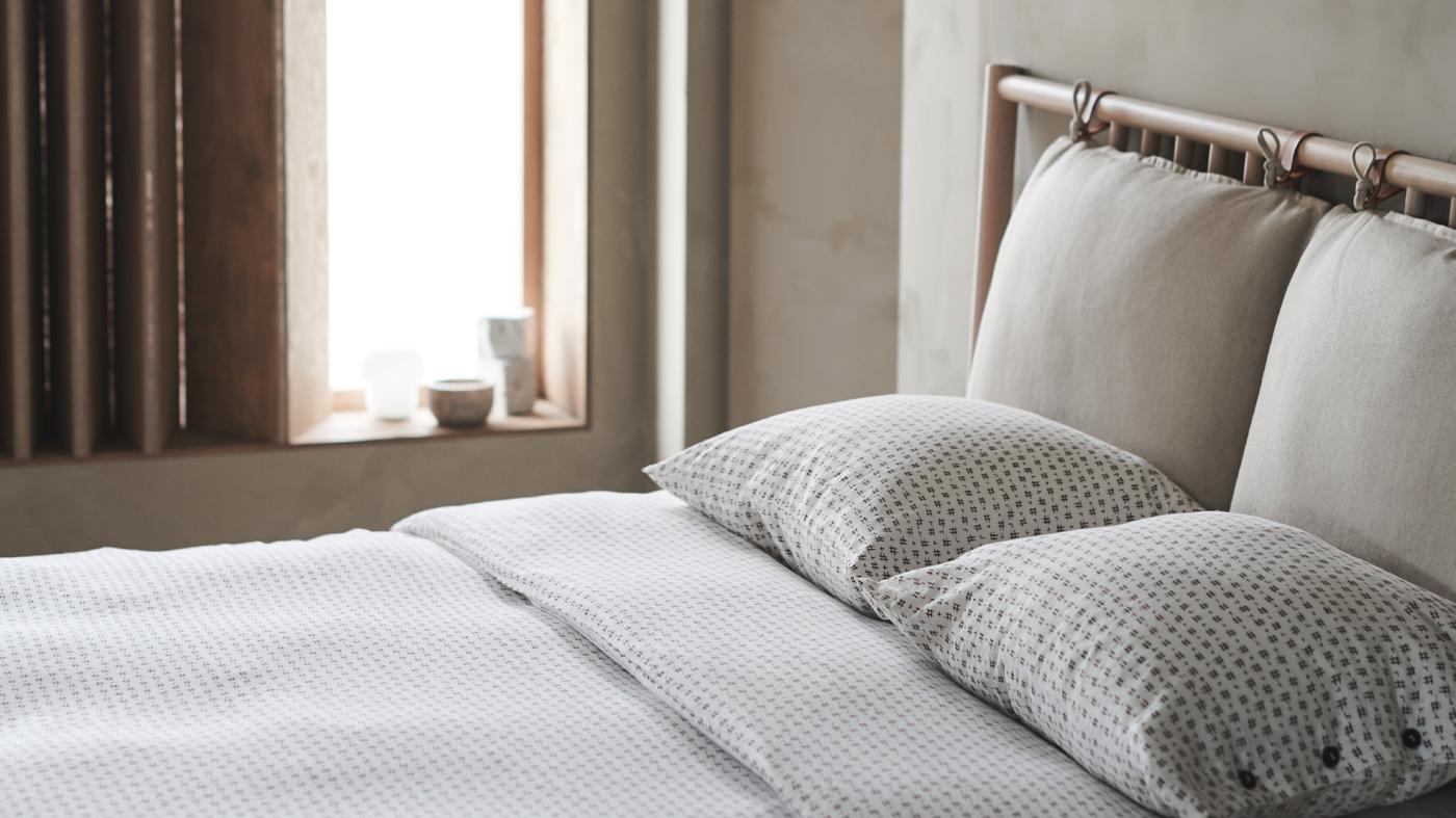 Dormitorio apacible en colores neutros iluminado por la luz del día con una cama doble con funda nórdica y funda de almohada VÄGTÅG.