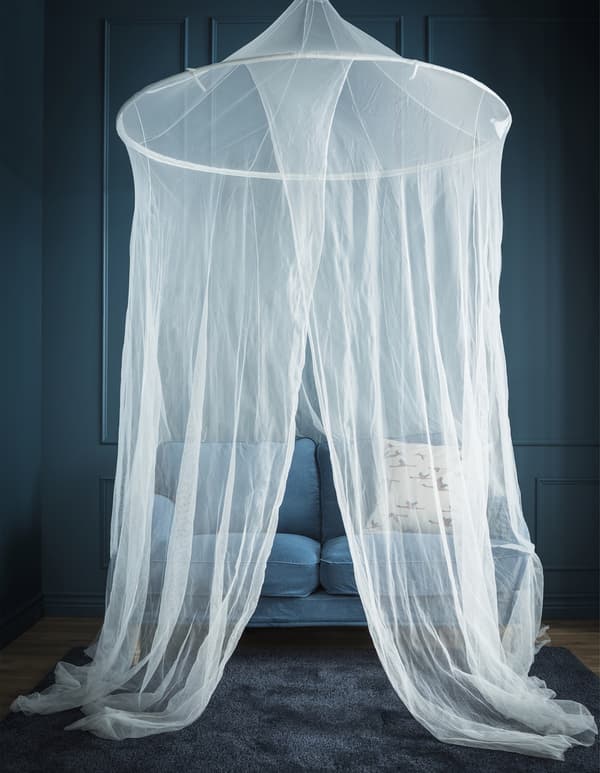 Dormitorio azul con dosel de red colgado encima de un pequeño sofá azul.