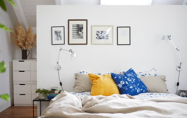 Dormitorio branco con roupa de cama neutra e floreada, e unhas fotos en branco e negro na parede.