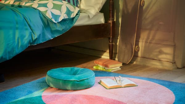 Dormitorio con la serie de textiles GRACIÖS en tonos turquesa, que incluye una funda nórdica, una alfombra estampada y un cojín redondo de terciopelo.