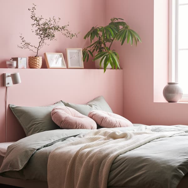 Dormitorio con paredes rosadas, una cama con cojines y mantas en tonos rosados.