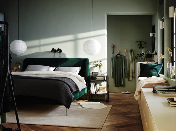 Dormitorio con una cama tapizada en verde oscuro TUFJORD , 2 lámparas colgantes blancas, ropa de cama blanca y una manta gris.