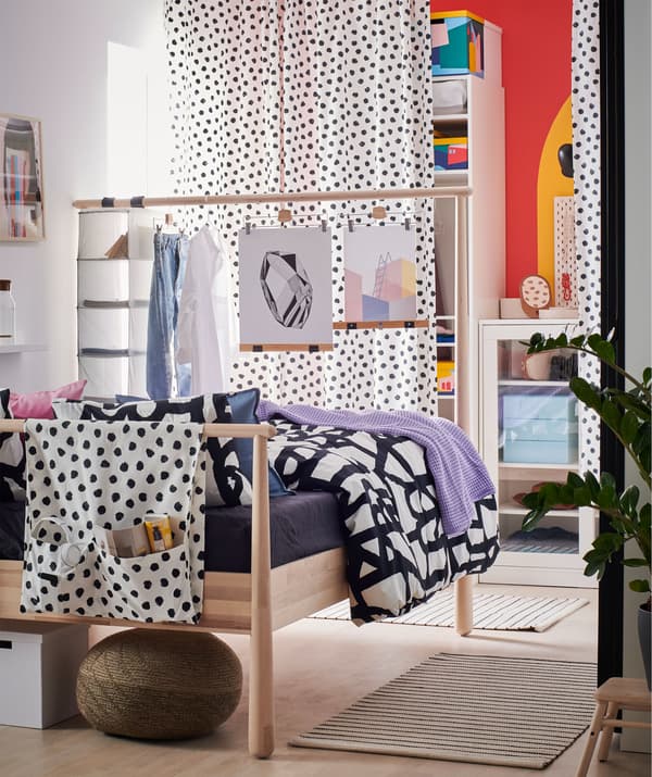 Dormitorio cunha parede ao fondo, detrás das cortinas, con almacenamento aberto e pechado. O cabeceiro alto da cama actúa como separador de espazos.