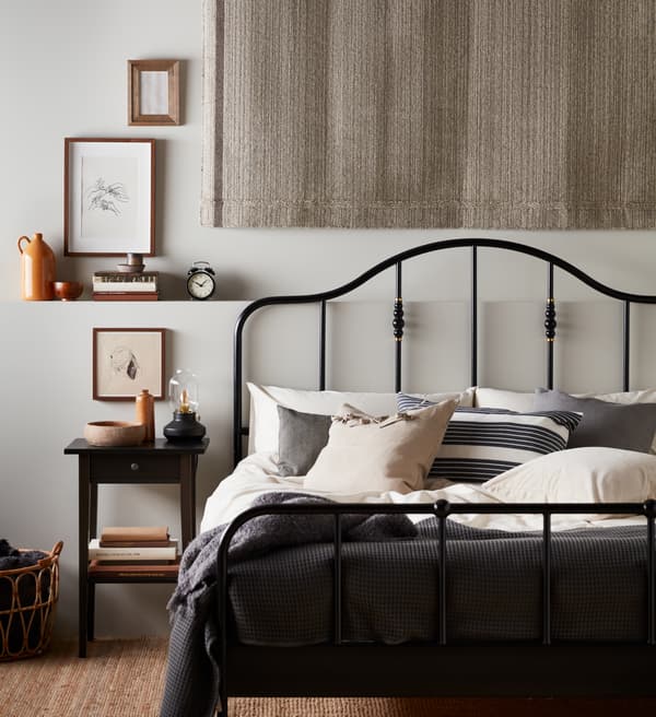 Dormitorio de estilo escandinavo tradicional de IKEA con una cama negra de hierro forjado, una mesilla de noche negra de madera y una lámpara tipo quinqué.