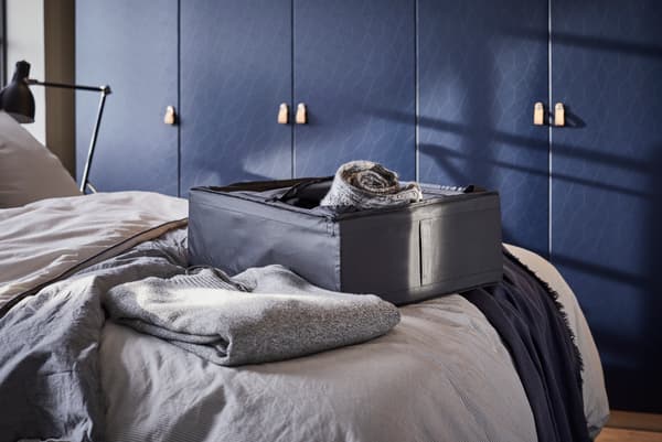 Dormitorio de IKEA con una caja de ropa gris encima de la cama.
