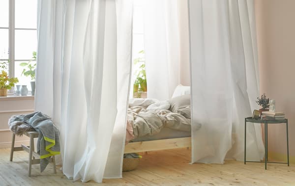 Dormitorio luminoso con una cama con dosel hecho con cortinas blancas y el sistema de rieles VIDGA de IKEA.