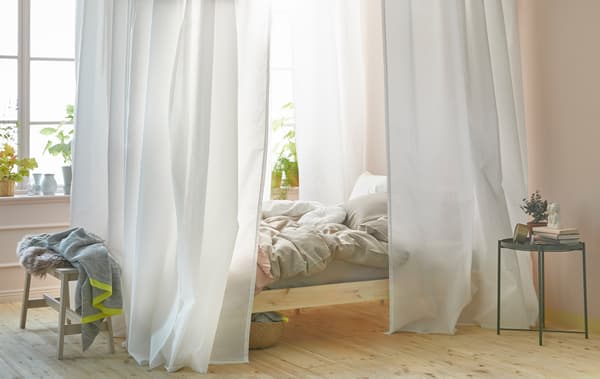 Dormitorio luminoso cunha cama con dosel feito con cortinas brancas e o sistema de guías VIDGA de IKEA.