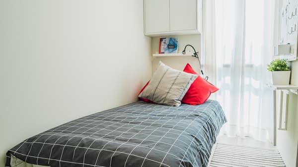 Dormitorio secundario con cama simple con cubreplumon azul con lineas blancas y dos cojines, uno rojo y uno beige.