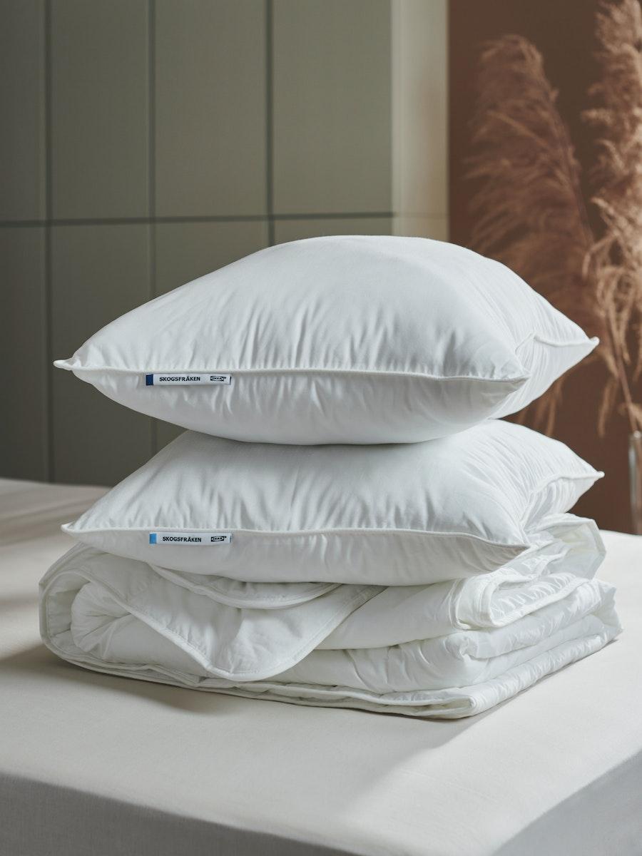 Dos almohadas SKOGSFRÄKEN blancas apiladas una sobre la ora sobre ropa de cama IKEA