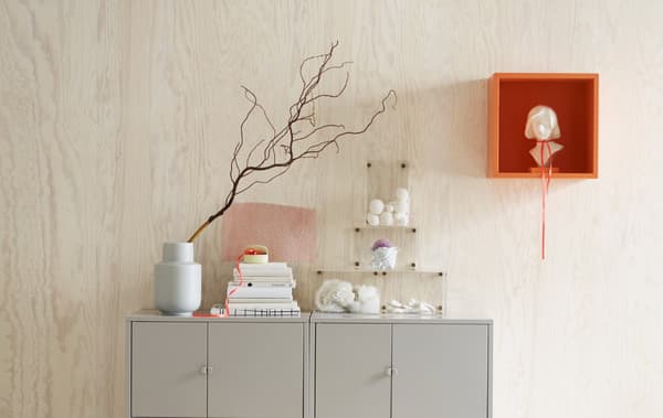Dos armarios grises frente a una pared de pino con una iluminación natural, incluido un armario montado en pared EKET naranja con una figura.