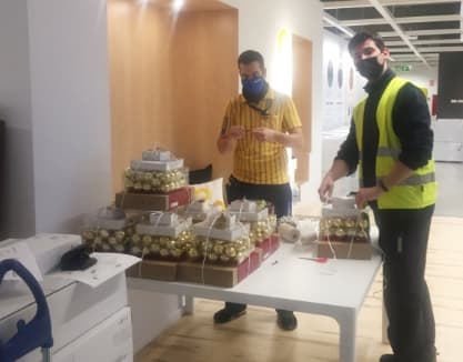 Dos empleats preparen accessoris per a les persones més desfavorides, col·laborant en una acció solidària.
