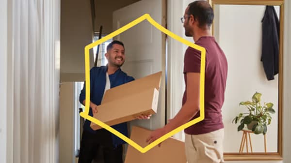 Dos hombres intercambian cajas de cartón mientras sonríen, enmarcados por una forma hexagonal amarilla.