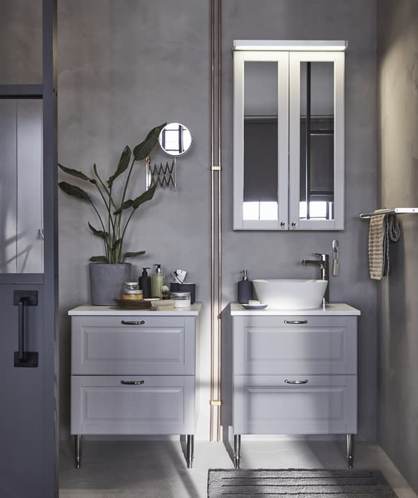 Dos módulos de almacenaje para baño en gris, uno con lavabo, y un armario con espejo frente a la pared gris.