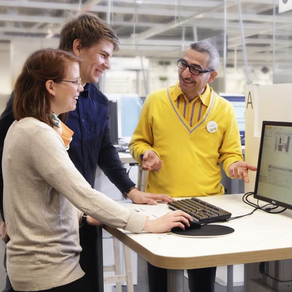 Dos personas manejando un programa de un computador acompañados por un colaborados IKEA.
