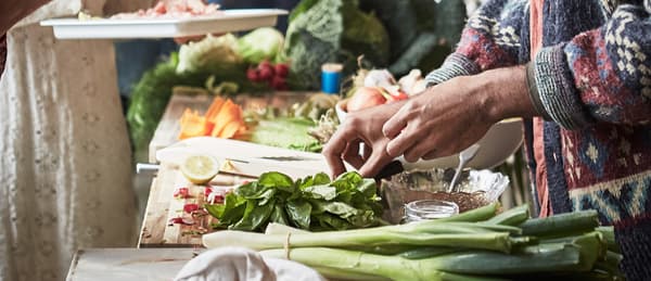 Dos personas preparando una ensalada con puerros, hojas de espinaca, zanahorias y col.