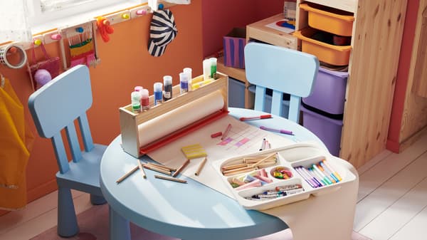 Dos sillas infantiles y una mesa infantil de la serie MAMMUT en azul claro. Hay material artístico en la mesa.