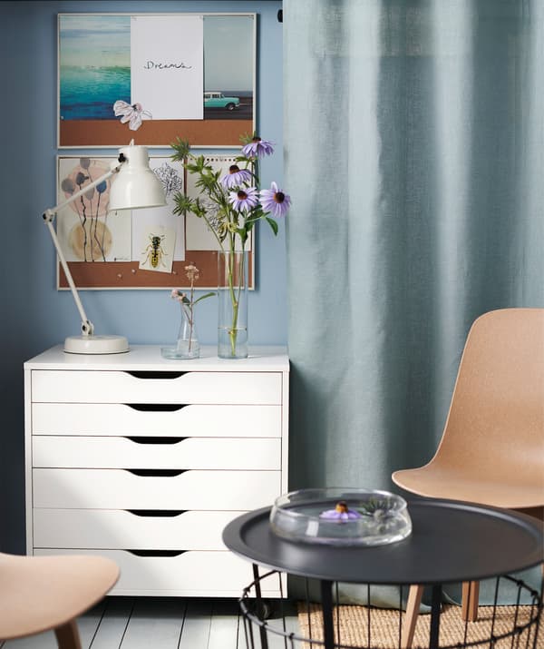 Dos sillas junto a una mesa de café, con un armario ALEX blanco contra la pared, en una habitación de color azul.