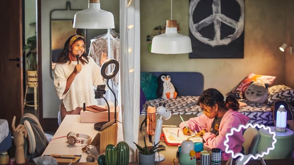 Două adolescente la birouri ALEX așezate față în față. Una studiază, iar cealaltă înregistrează în fața lămpii LÅNESPELARE.