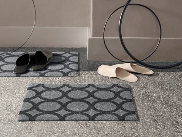 Două covorașe gri IKEA MAILS cu un model negru de cercuri. Sunt fabricate din sticle PET reciclate.