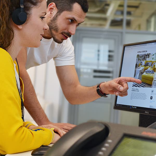 Două persoane privesc un monitor de computer, una indicând ecranul. Identitățile sunt ascunse.