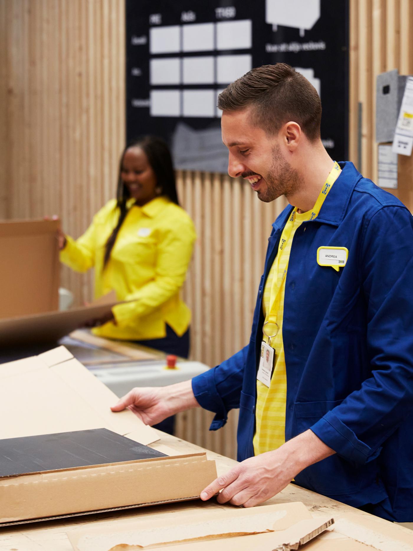 Dous colaboradores/as de IKEA, unha cunha camisa amarela e outro cunha chaqueta azul, empaquetando artigos en embalaxes de cartón.