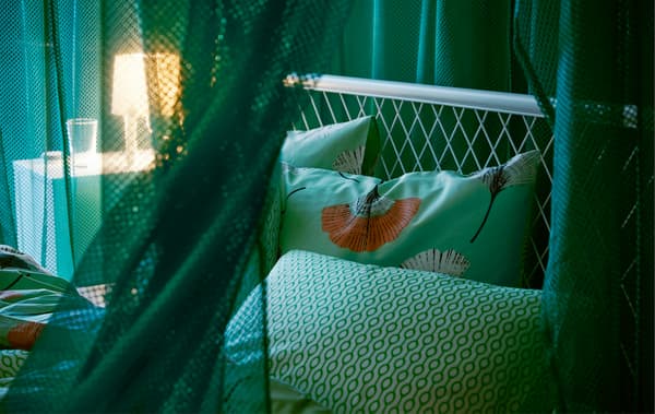 Draped green IKEA GRÅTISTEL net curtains in a bedroom, creating a room in the room, while letting through a little light.