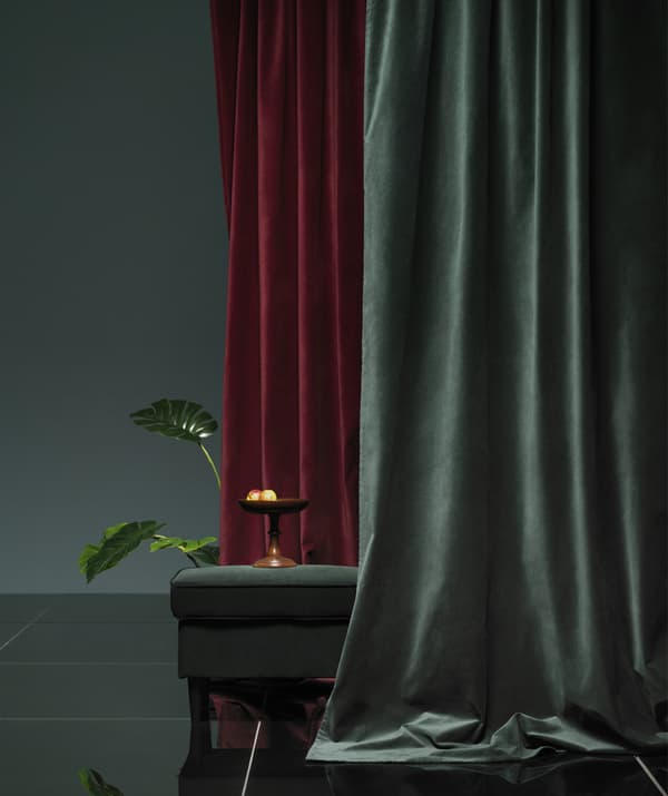 Drappeggio di tende in velluto rosso scuro e verde intorno a un poggiapiedi.