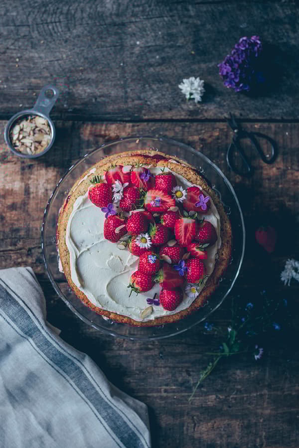 Draufsicht auf den Kuchen, wie er mit Erdbeeren verziert wird.