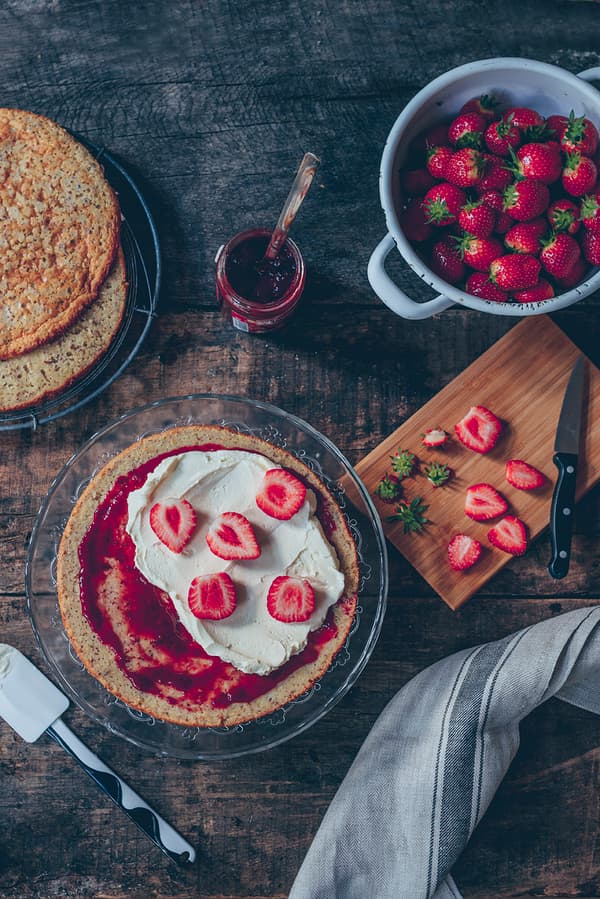 Draufsicht auf den Kuchen, wie er mit Erdbeeren verziert wird.