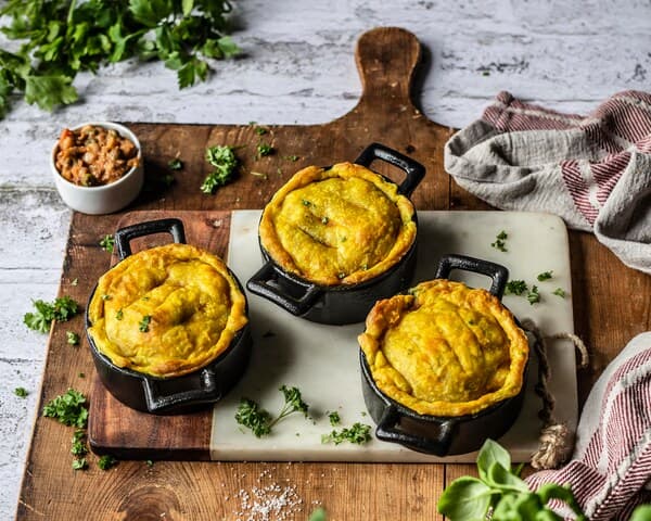 Drei Auflaufformen mit gold-braun gebackenen veganen Hack-Pies.