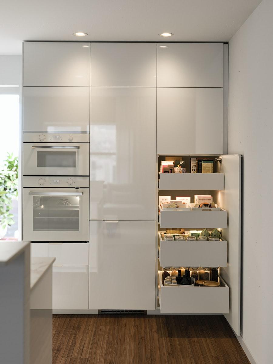 Drei Hochschränke mit RINGHULT hochglanz weißen Fronten. In einem Schrank sieht man Backofen und Mikrowelle, ein Schrank ist geöffnet und man sieht vier MAXIMERA Schubladen.