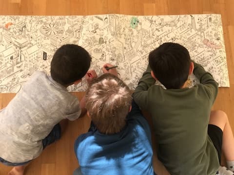 Drei Kinder malen zusammen an einem grossen Ausmalbild