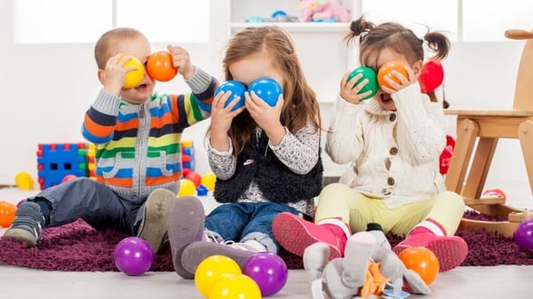 Drei Kinder sitzen auf einem Teppich und spielen mit bunten Bällen